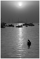Man fishing from rowboat and anchored yachts, sunrise. Mumbai, Maharashtra, India ( black and white)