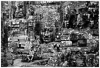 Boy sits next to large stone smiling faces, the Bayon. Angkor, Cambodia (black and white)