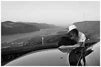 Couple embracing on car hood, with view of mouth of river gorge. Columbia River Gorge, Oregon, USA ( black and white)