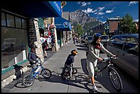 Woman and kids with mountain bikes on downtown Banff sidewalk. Banff National Park, Canadian Rockies, Alberta, Canada (color)