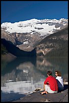Couple sitting in the sun in front of Lake Louise, morning. Banff National Park, Canadian Rockies, Alberta, Canada (color)