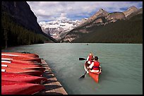 Canoeists paddling out of the boat dock in blue-green waters, Lake Louise, morning. Banff National Park, Canadian Rockies, Alberta, Canada (color)