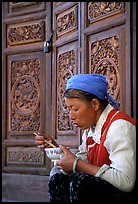 Bai woman eating from a bowl in front of carved wooden doors. Dali, Yunnan, China ( color)