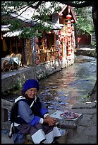 Elderly naxi woman peddles candies near a canal. Lijiang, Yunnan, China