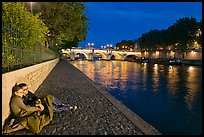 Couple sitting on quay on banks of the Seine River. Paris, France