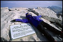 Hiker laying exhausted on Mt Whitney summit sign. Sequoia National Park, California (color)