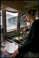 Woman cooking eggs aboard small tour boat, with glacier outside. Glacier Bay National Park ( color)