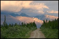 Gravel road leading to mountains lit by sunset light. Wrangell-St Elias National Park, Alaska, USA.