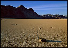 Tracks, moving stone on Racetrack playa and Ubehebe Peak, late afternoon. Death Valley National Park, California, USA. (color)