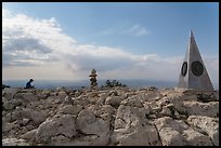 Hiker sitting on Guadalupe Peak summit with cairn and monument. Guadalupe Mountains National Park, Texas, USA. (color)