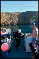 Woman diver stepping onto boat and Annacapa Island. Channel Islands National Park, California, USA. (color)