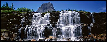 Waterfall flowing over dark rock and peak. Glacier National Park, Montana, USA.