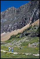 Couple hiking on trail amongst wildflowers near Hidden Lake. Glacier National Park, Montana, USA. (color)
