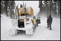 Couple standing in snowdrift next to snow coach. Yellowstone National Park, Wyoming, USA. (color)