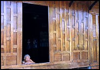 Woman looks out of teak house window. Damnoen Saduak, Thailand
