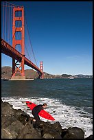 Surfer scrambling on rocks below the Golden Gate Bridge. San Francisco, California, USA (color)