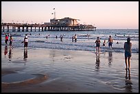 Beachgoers near Santa Monica Pier reflected in wet sand, sunset. Santa Monica, Los Angeles, California, USA (color)