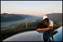 Couple embracing on car hood, with view of mouth of river gorge. Columbia River Gorge, Oregon, USA (color)