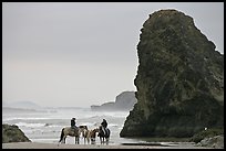 Women ridding horses next to sea stack. Bandon, Oregon, USA (color)