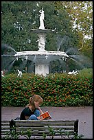 Woman sitting on bench with book in front of Forsyth Park Fountain. Savannah, Georgia, USA (color)