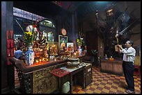 Man in prayer, with fierce statue of general behind, Jade Emperor Pagoda, district 3. Ho Chi Minh City, Vietnam (color)