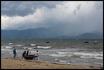 Men pushing coracle boat into stormy ocean. Da Nang, Vietnam ( color)