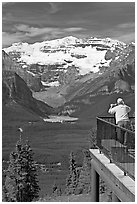 Man looking at Lake Louise through binoculars on observation platform. Banff National Park, Canadian Rockies, Alberta, Canada (black and white)
