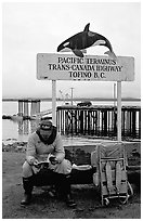 Backpacker sitting under the Transcanadian terminus sign, Tofino. Vancouver Island, British Columbia, Canada (black and white)