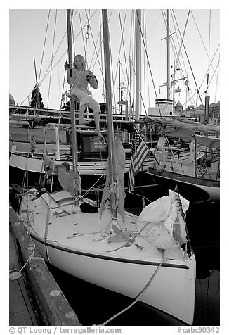 Girl swinging from the mast of a small sailboat, Inner Harbour. Victoria, British Columbia, Canada (black and white)
