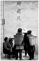 Elderly women with back baskets in front of a wall with Chinese scripture. Shaping, Yunnan, China ( black and white)