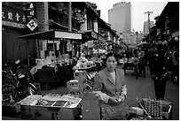 Street market in an old alley of wooden buildings, with a high rise in the background. Kunming, Yunnan, China ( black and white)