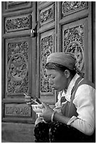 Bai woman eating from a bowl in front of carved wooden doors. Dali, Yunnan, China ( black and white)