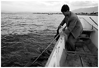 Cormorant fisherman catches one of his birds to retrieve the fish it caught. Dali, Yunnan, China (black and white)
