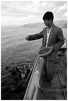 Cormorant fisherman feeds small fish to his birds as a prize for catching large fish. Dali, Yunnan, China (black and white)