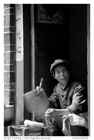 Naxi woman at doorway selling broiled corn. Lijiang, Yunnan, China (black and white)