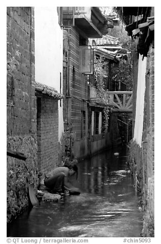 Woman washes clothes in the canal. Lijiang, Yunnan, China (black and white)