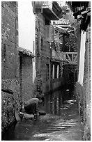 Woman washes clothes in the canal. Lijiang, Yunnan, China (black and white)