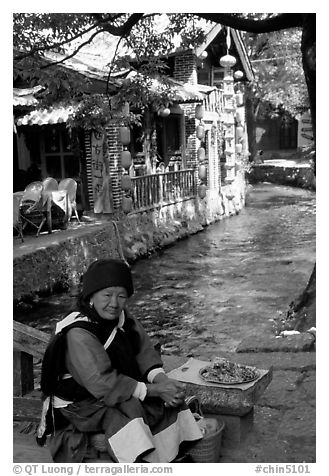 Elderly naxi woman peddles candies near a canal. Lijiang, Yunnan, China (black and white)