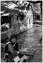 Elderly naxi woman peddles candies near a canal. Lijiang, Yunnan, China (black and white)