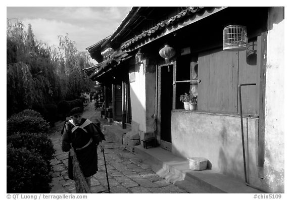 Naxi woman sweeps the floor at the door of her wooden house. Lijiang, Yunnan, China