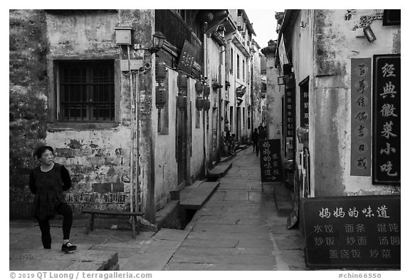 Woman standing next to main street. Xidi Village, Anhui, China (black and white)