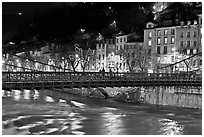 Suspension bridge at night with Christmas lights reflected in river. Grenoble, France ( black and white)