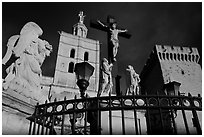 Cross with Christ, statues, and towers, evening light. Avignon, Provence, France ( black and white)