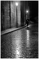 Street lamps reflected in wet pavement, with woman walking. Paris, France ( black and white)