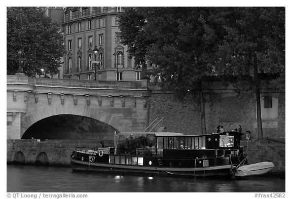 Lighted live-in barge, quay, and Pont-Neuf. Paris, France