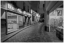 Narrow cobblestone street and businesses at night, Montmartre. Paris, France ( black and white)