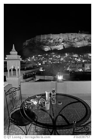 Rooftop restaurant table with food served and view of Mehrangarh Fort by night. Jodhpur, Rajasthan, India (black and white)
