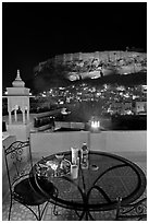 Rooftop restaurant table with food served and view of Mehrangarh Fort by night. Jodhpur, Rajasthan, India (black and white)