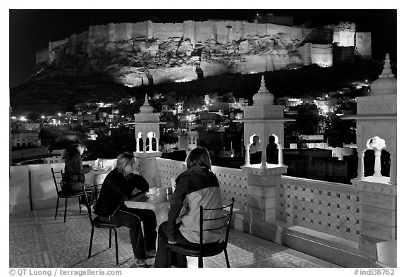 Travelers on rooftop terrace with view of Mehrangarh Fort by night. Jodhpur, Rajasthan, India