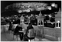 Travelers on rooftop terrace with view of Mehrangarh Fort by night. Jodhpur, Rajasthan, India (black and white)